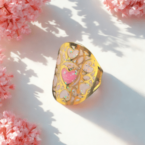 Bague Cœur en Lumière rose pailletée Cœur Enchanteur finition dorée posée sur table