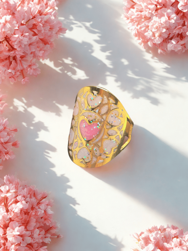 Bague Cœur en Lumière rose pailletée Cœur Enchanteur finition dorée posée sur table