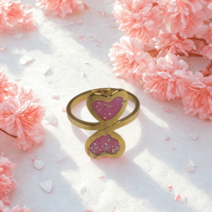 Bague duo Cœur en Lumière rose pailletée Double Tendresse finition dorée posée sur table