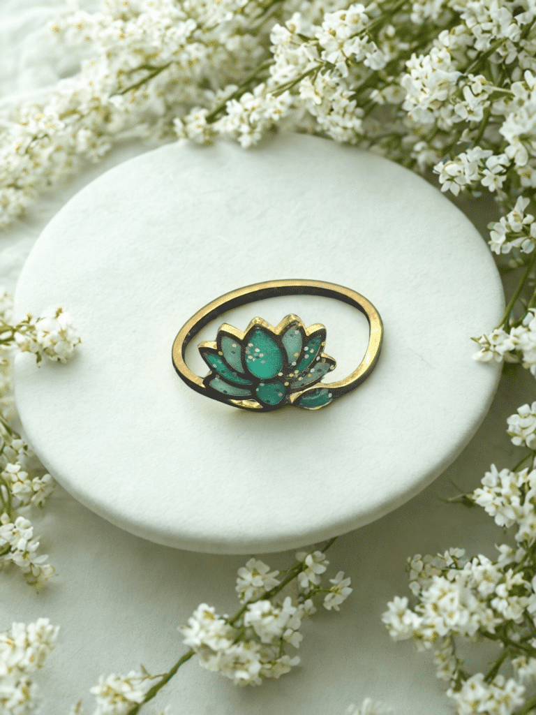 Bague Lotus Sacré vert pailletée Lotus Émeraude finition dorée posée sur table