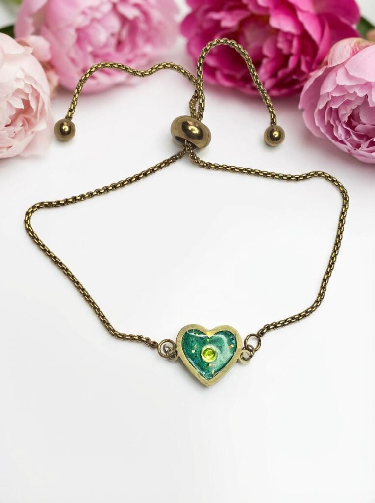 Bracelet Cœur en Lumière vert pailleté Éclat du Cœur finition dorée posé sur table