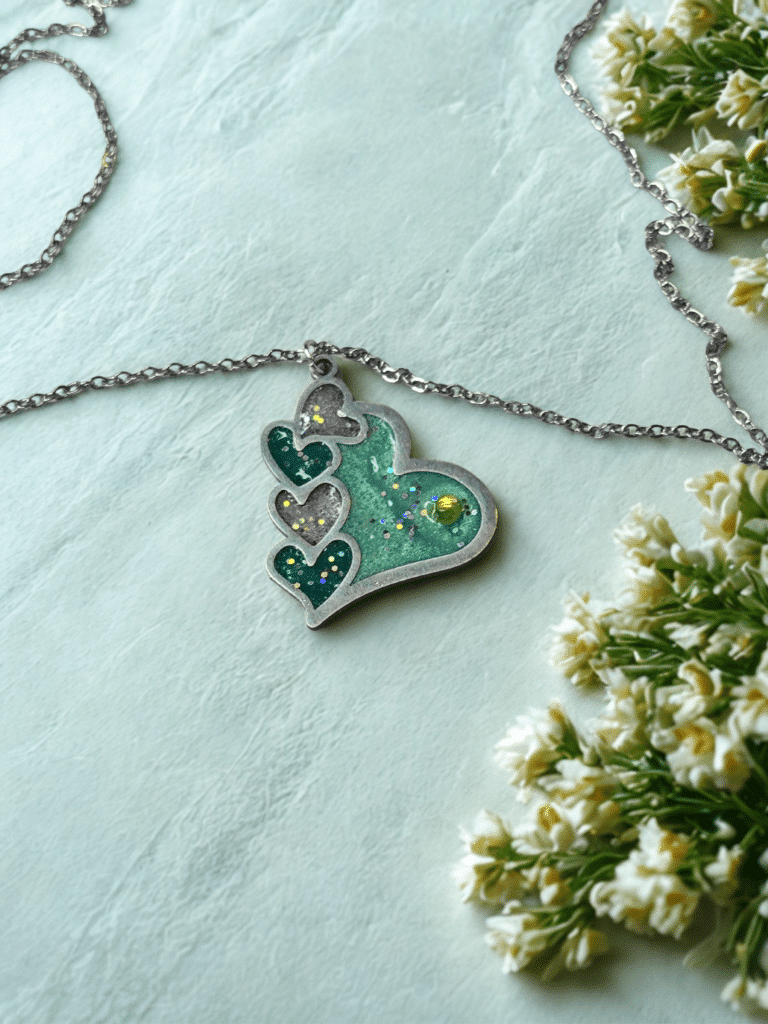 Collier Cœur en Lumière vert pailleté Cœur Émeraude finition argentée posé sur table