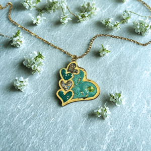 Collier Cœur en Lumière vert pailleté Cœur Émeraude finition dorée posé sur table