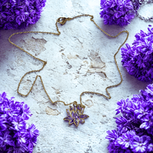 Collier Lotus Sacré violet pailleté Âme en Fleur finition dorée posé sur table