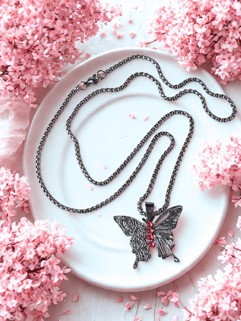 Collier Papillon Éternel argenté Envol Céleste posé sur assiette entourée de fleurs roses