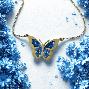Collier Papillon Éternel bleu pailleté Aile Céleste finition dorée posé sur table