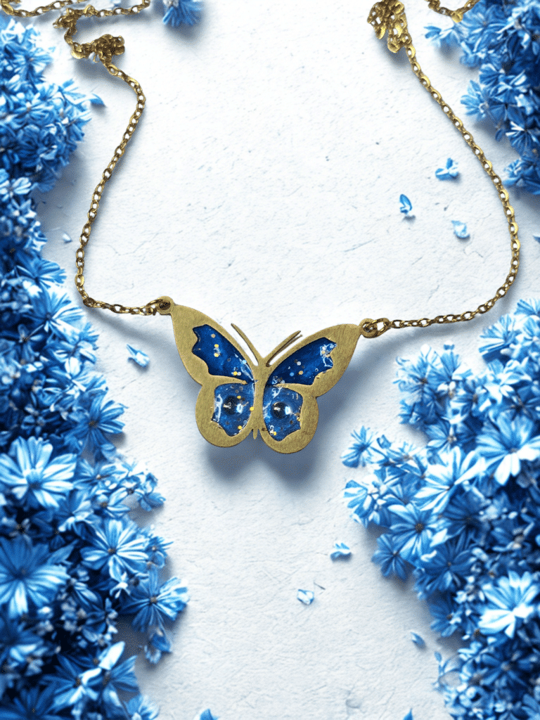 Collier Papillon Éternel bleu pailleté Aile Céleste finition dorée posé sur table