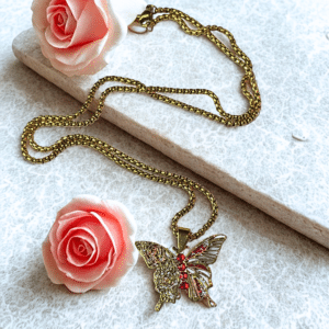 Collier Papillon Éternel doré Ailes de Feu posé sur support pierre avec roses