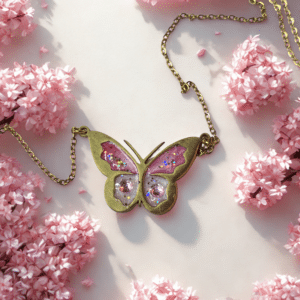 Collier Papillon Éternel rose pailleté Aile Enchantée finition dorée posé sur table