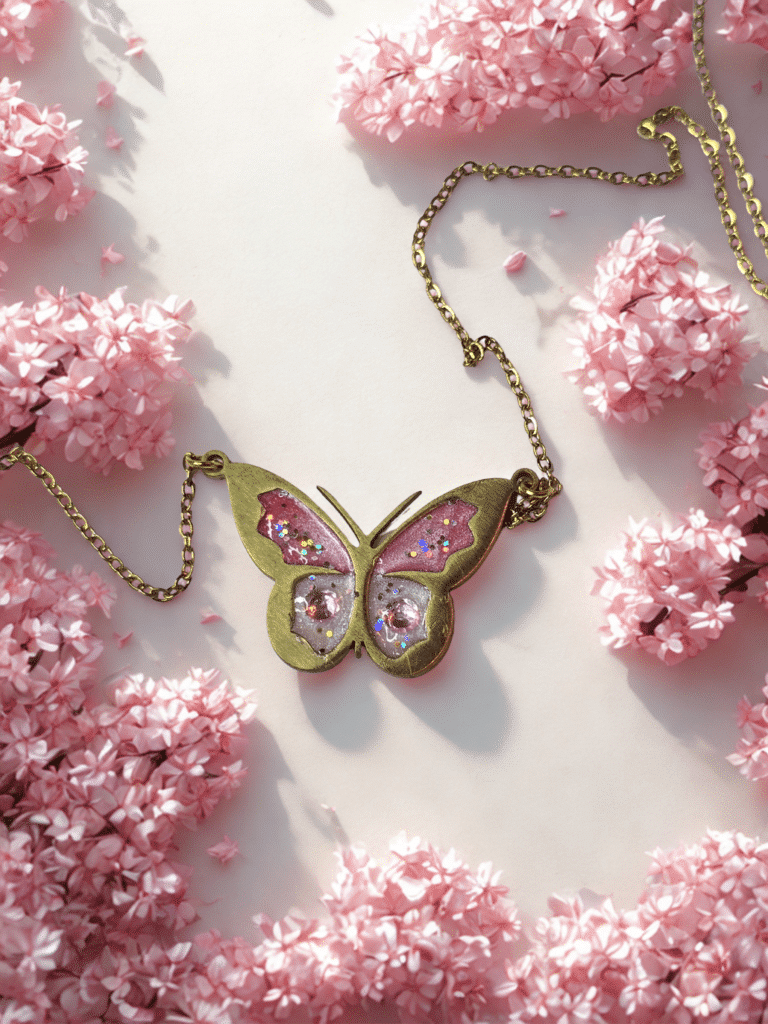 Collier Papillon Éternel rose pailleté Aile Enchantée finition dorée posé sur table
