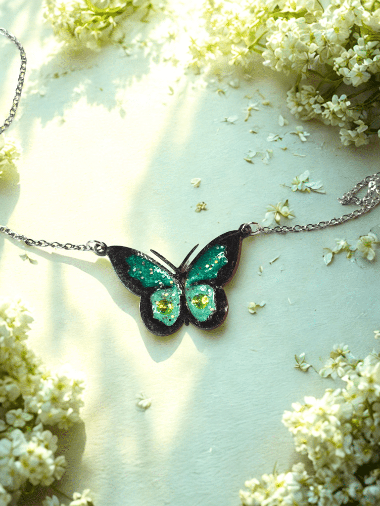 Collier Papillon Éternel vert pailleté Aile Émeraude finition argentée posé sur table