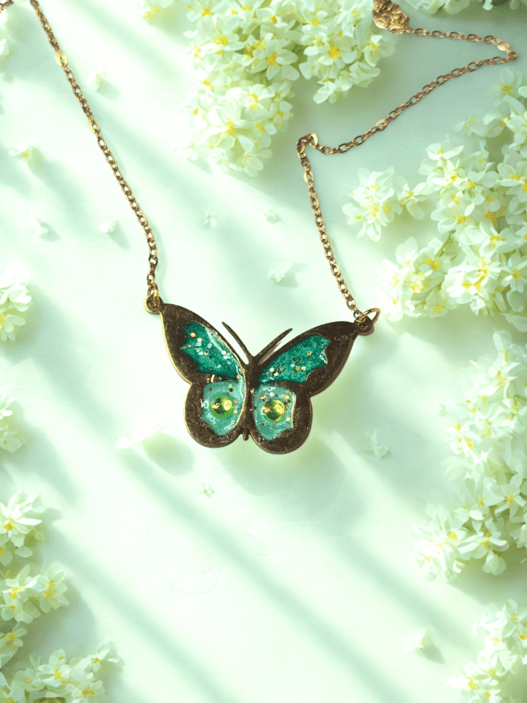 Collier Papillon Éternel vert pailleté Aile Émeraude finition dorée posé sur table