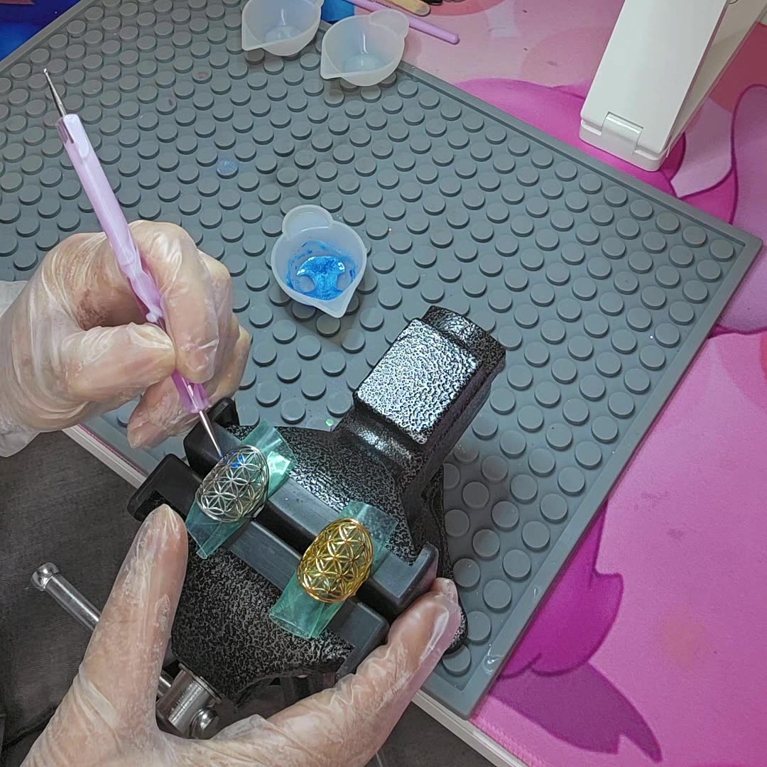 Fabrication de bijoux artisanaux Jewels Spirit : application de résine pailletée au pinceau sur des bagues Fleur de Vie